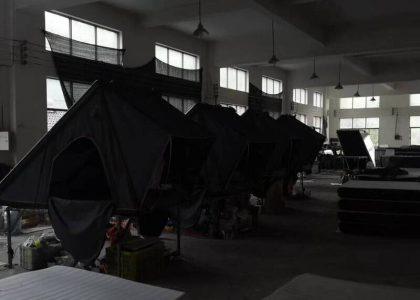 Hard shell rooftop tent displayed in low-light factory setting to show profile.