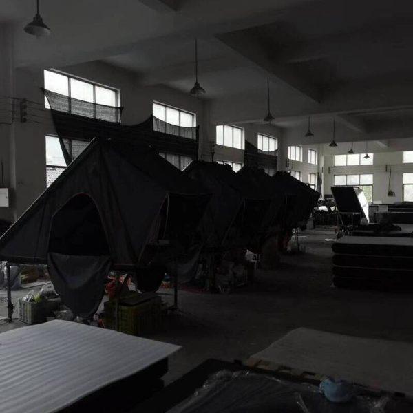 Hard shell rooftop tent displayed in low-light factory setting to show profile.